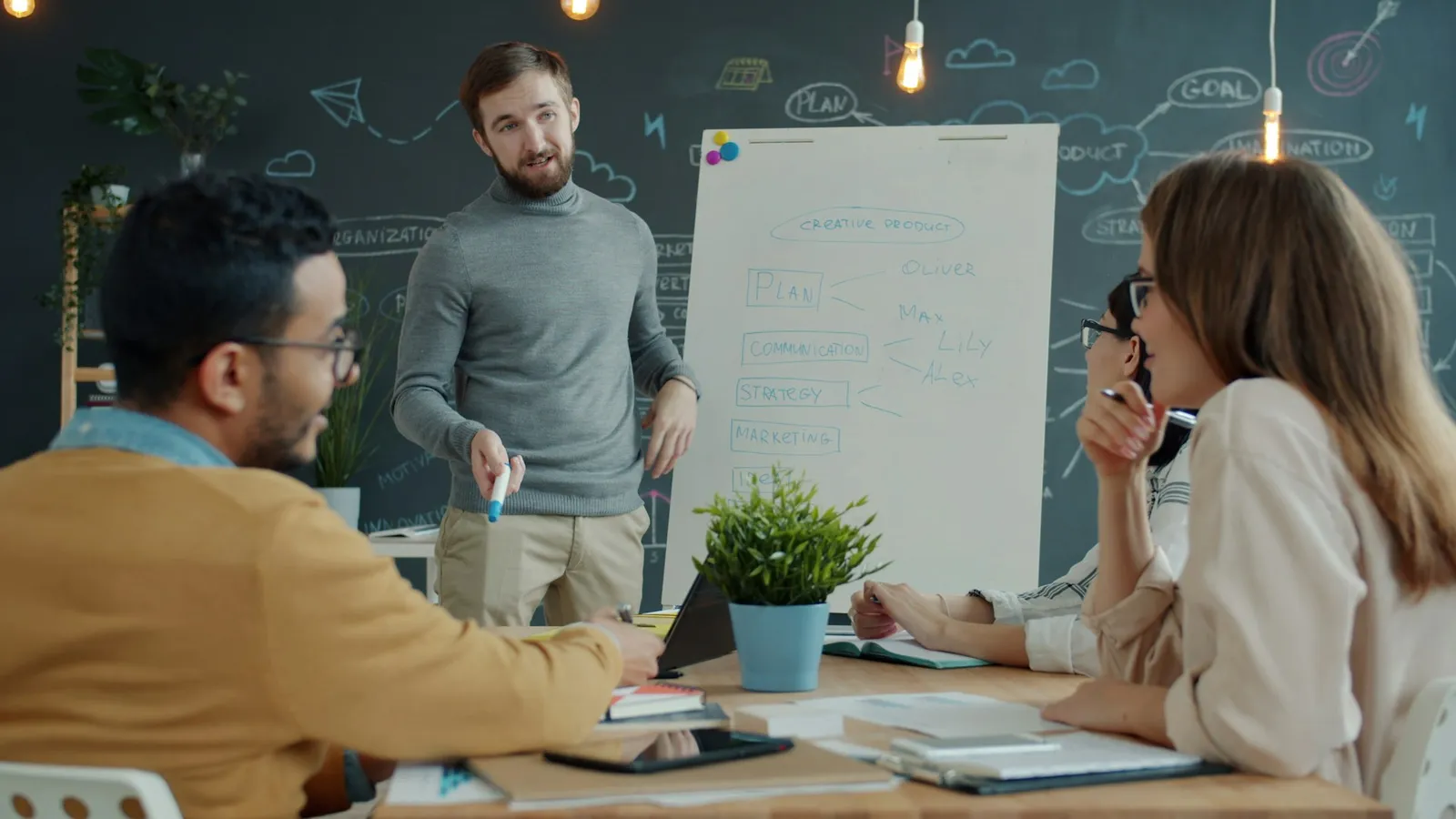 Team gathered around a whiteboard in a bright modern office as one person points to handwritten notes while colleagues look on and discuss