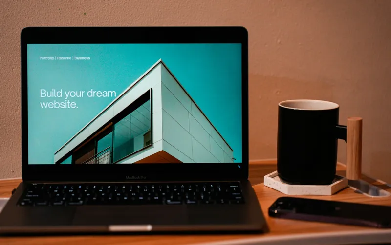 Open MacBook on a warm wooden desk with a white coffee mug placed beside it in a quiet home workspace