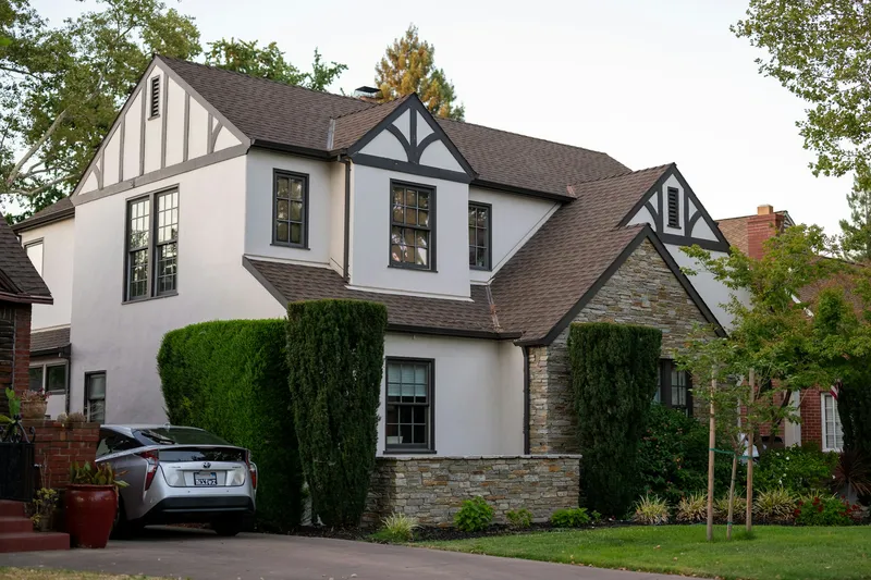 Front view of a single-family suburban home with a freshly planted shade tree on the front lawn and a car parked in the driveway