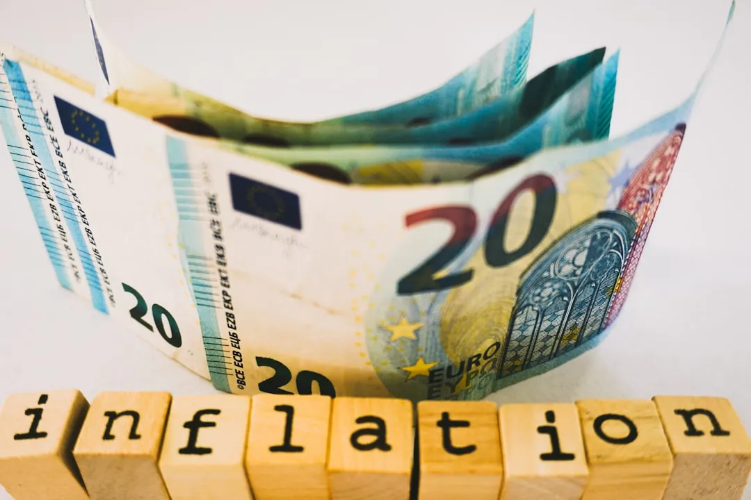 A thought-provoking still life featuring a rolled 20 euro banknote with its vibrant colors and security details prominently displayed. Below it, rustic wooden blocks spell out the word 'inflation,' creating a striking visual metaphor for the economic forces that impact currency value. The clean white background and soft lighting draw attention to the contrast between the crisp, modern banknote and the raw texture of the blocks—ideal for discussions on finance, economics, or educational content about monetary policy.