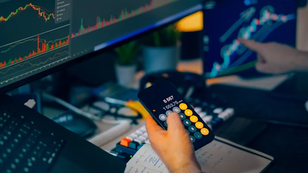 Financial trading workstation stock crypto investment analysis. Closeup hand holding smartphone calculator desk monitors charts candlesticks graphs market data savings portfolio planning risk management economy finance technology office night lighting focus strategy performance growth profit volatility currency bitcoin ethereum exchange dashboard indicators keyboard notebook calculations