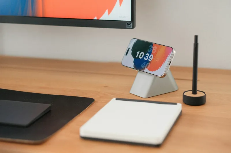 Smartphone, a blank notepad, and a pen arranged on a warm wooden desk in soft natural light