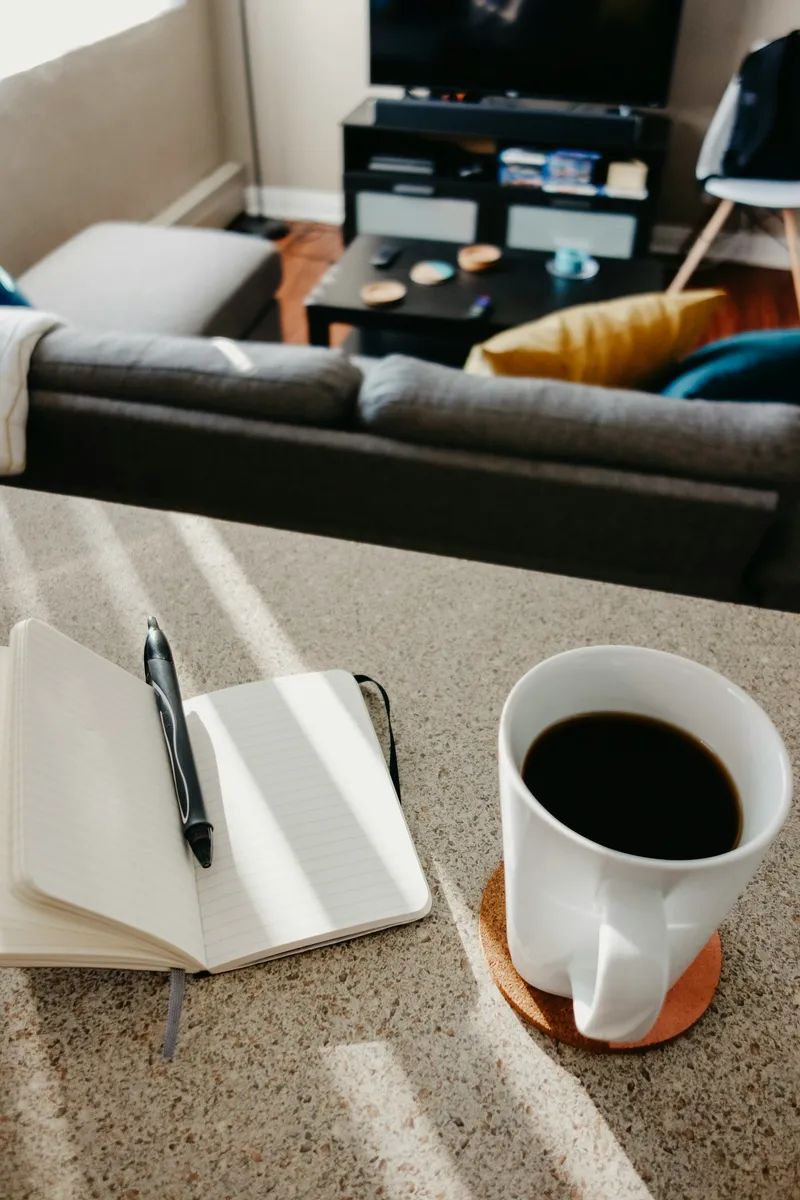 Black ceramic mug of coffee next to a black click pen resting on an open notebook in a quiet morning workspace